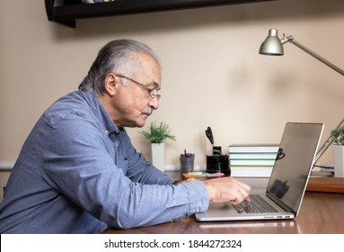 Senior Man Learn To Use Computer. Old Man In Glass And Blue Shirt Using A Laptop Computer For Online Studying At Home Office