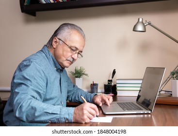 Senior Man Learn To Use Computer. Old Man In Glass And Blue Shirt Using A Laptop Computer For Online Studying At Home Office