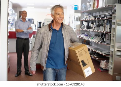 A Senior Man Leaving An Electrical Shop With A Box Under His Arm, Looking Happy