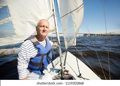 Senior Man In Lifejacket Sitting In Yacht And Enjoying Summer Weekend By Seaside