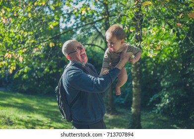 A Senior Man Is Lifting His Grandson Outside In Nature