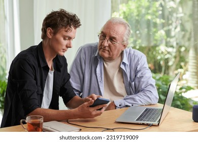 Senior man listening to grandson explaining how to use application on smartphone - Powered by Shutterstock