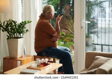 Senior Man Listening To Voice Message On Smartphone And Looking Outside At Entrance Gates Waiting For Guests