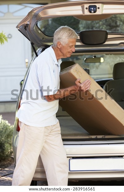 Senior Man\
Loading Large Package Into Back Of\
Car