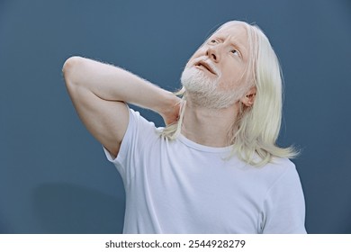 Senior man with long light hair and beard in a casual white t shirt, expressing serenity against a soft blue wall background Gentle pose evokes calmness and introspection - Powered by Shutterstock