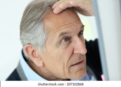 Senior Man Looking At Hair Loss In Mirror