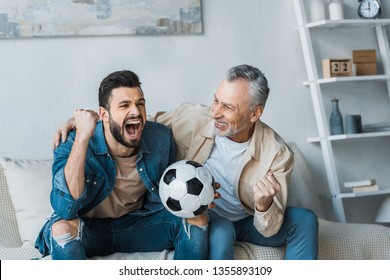 senior man looking at happy son cheering while watching championship and holding football 