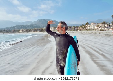 Senior man looking at the horizon carrying surfboard before getting into the water to surf the waves - Powered by Shutterstock