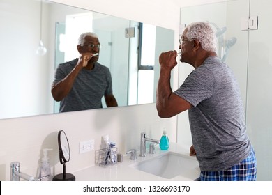 Senior Man Looking At Reflection In Bathroom Mirror Wearing Pajamas Brushing Teeth - Powered by Shutterstock