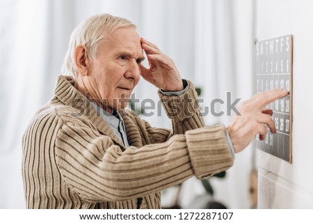senior man looking at wall calendar and touching head