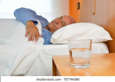 Senior man lying on bed with glass of mineral water on the nightstand - Powered by Shutterstock