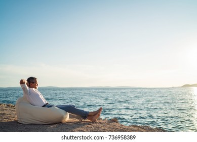 Senior Man Lying On Deck Chair On The Beach During Sunset