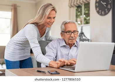 Senior Man And Mature Daughter Smiling And Looking At Laptop At Home. Happy Daughter Teaching And Showing New Computer Technology To Her Old Dfather. Old Man Learn To Use Computer.