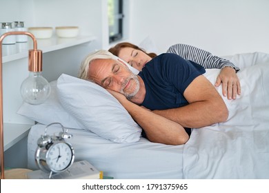 Senior Man And Mature Woman Sleeping Together In Their Bed. Married Middle Aged Couple Resting With Eyes Closed In The Morning. Wife Lying On Side Embracing Her Husband While Dreaming. 