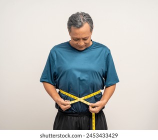 Senior man measuring waistline with measure tape. Weight loss diet session. Old man in sportswear fit and firm body shape. Care about eating and workout exercise. - Powered by Shutterstock