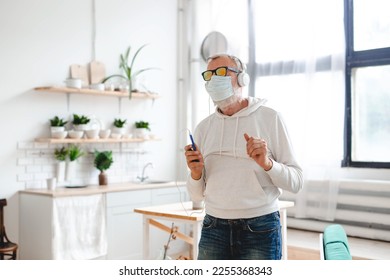 Senior man with medical mask on face dance and using smartphone app for creating playlist music on mobile app - Elderly male having fun dancing with mobile phone technology - Tech and joyful elderly - Powered by Shutterstock