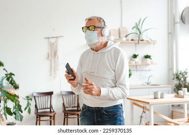 Senior man with medical mask on face dance and using smartphone app for creating playlist music on mobile app - Elderly male having fun dancing with mobile phone technology - Tech and joyful elderly - Powered by Shutterstock