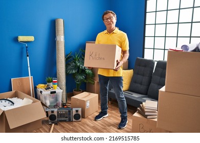 Senior man moving to a new home holding cardboard box clueless and confused expression. doubt concept. 