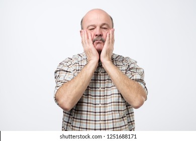 Senior man with mustache covering face with both hands, feeling stressed out as he deleted all files on computer.