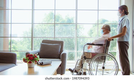 Senior Man At The Nursing Home Concept. A Female Nurse Stands Holding A Wheelchair With An Elderly Person Sitting With The Nursing Home Care.