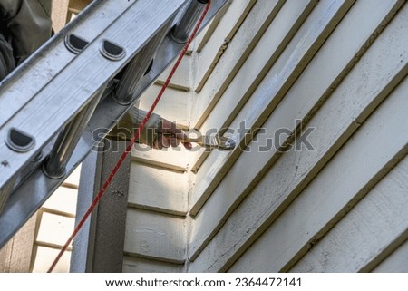 Senior man on an extension ladder painting sealer on wood siding of the exterior of a residential building

