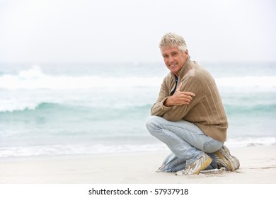 Senior Man On Holiday Kneeling On Winter Beach