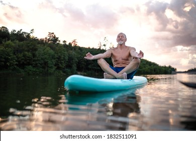 Senior Man On Paddleboard On Lake In Summer, Doing Yoga Exercise.