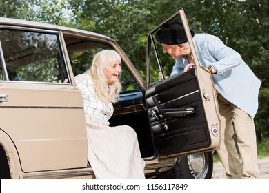 Senior Man Opening Car Door In Front Of Beautiful Woman