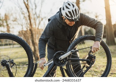 A senior man is outdoors on a sunny day, focused on fixing his mountain bike, using tools to repair the bike. - Powered by Shutterstock