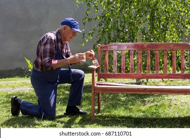 Senior man in overalls painting old bench in garden after sandblasting. Repairing old furniture - Powered by Shutterstock