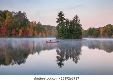 Senior man paddles a red canoe on a beautiful northern Minnesota lake with a small island at dawn during autumn - Powered by Shutterstock