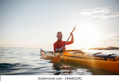 Senior Man Paddling Kayak On The Sunset Sea
