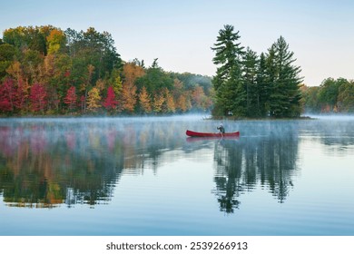 Senior man paddling a red wooden canoe on a beautiful northern Minnesota lake with a small island at dawn during autumn - Powered by Shutterstock