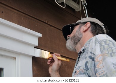 A senior man painting the doorway with white paint