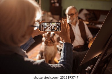 Senior man painting with his dog while being photographed at home - Powered by Shutterstock