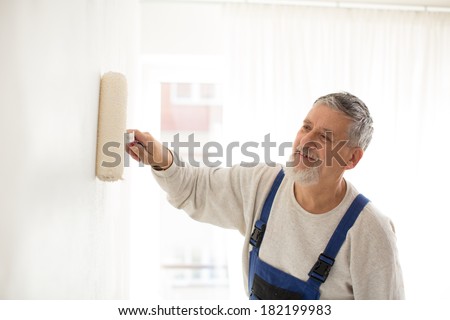 Senior man painting a wall in his home, smiling, enjoying the work