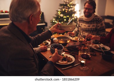 Senior Man Passing Food To Her Son On Dinner Table. Family Having Delicious Thanksgiving Dinner At Home.