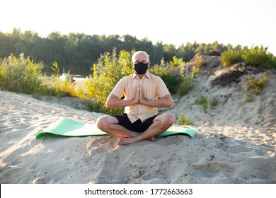 Senior Man Pensioner Wearing Protective Mask Sitting In Nature, Doing Yoga Exercise.