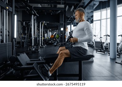 Senior man performs rowing exercise at modern gym