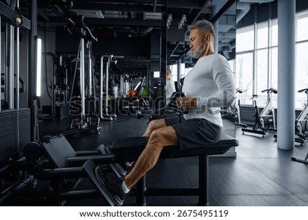 Senior man performs rowing exercise at modern gym