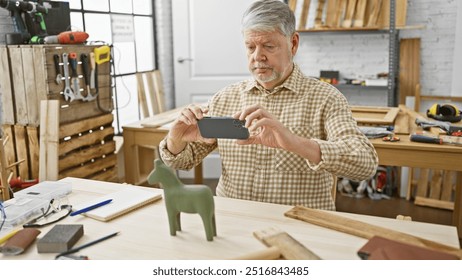 A senior man photographs a wooden figurine with his smartphone in a well-equipped carpentry workshop. - Powered by Shutterstock