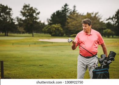 Senior man picking up golf club from bag at golf course. Mature male golfer picks his club for the next play.