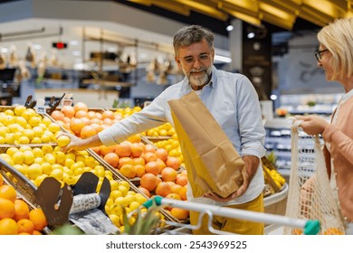 Senior man picking lemons in a paper bag, shopping with his wife in the fruit section of a grocery store, choosing healthy and fresh products - Powered by Shutterstock