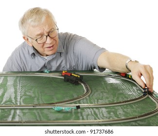 A Senior Man Placing An Engine On The Track As He Sets Up A New N-gauge Train Set.  Focus Is On The Man.  On A White Background.