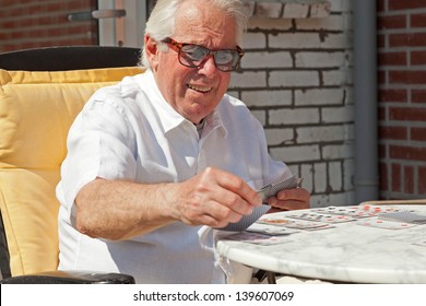 Senior Man Playing Card Game Outdoor In Garden.