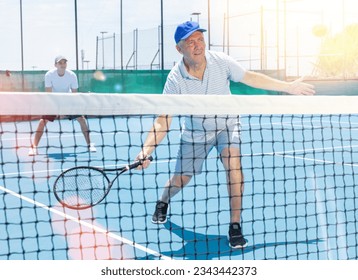 Senior man playing tennis on court holding tennis racket. Retirement retreat and active senior lifestyle concept. - Powered by Shutterstock