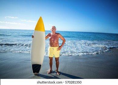 Senior man posing with a surfboard at the beach - Powered by Shutterstock