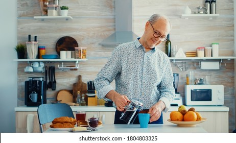 Senior man pouring hot coffee from french press in kitchen during breakfast. Elderly person in the morning enjoying fresh brown cafe espresso cup caffeine from vintage mug, filter relax refreshment - Powered by Shutterstock