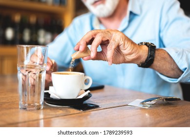 Senior Man Pouring Sugar Into Coffee At Restaurant