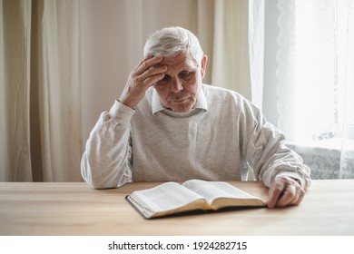 Senior Man Praying, Reading  An Old Bible In His Hands.